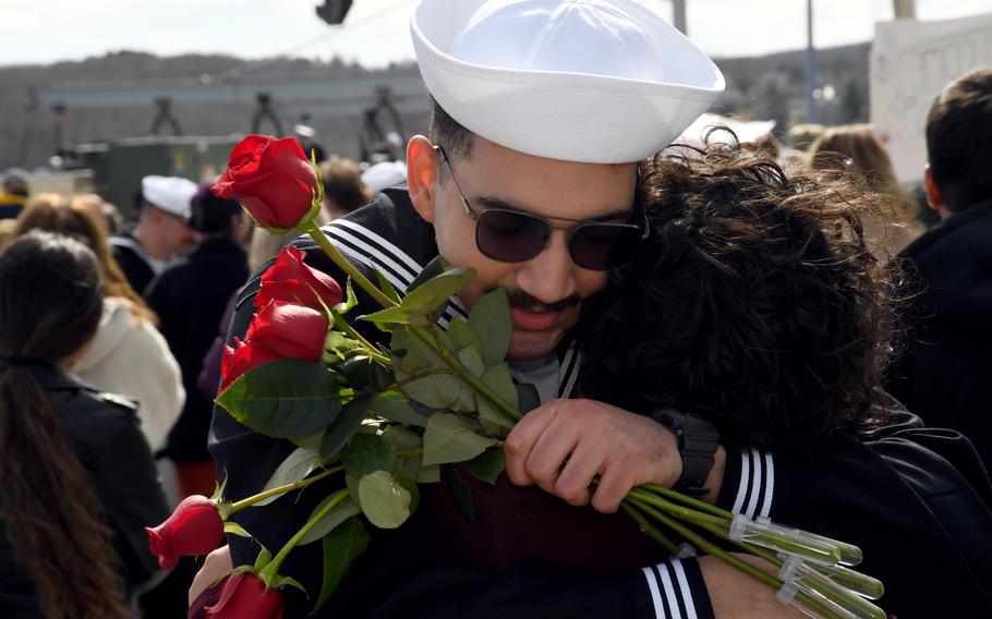 A sailor holds roses and hugs a woman.