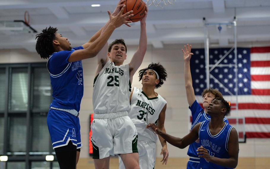 Naples' Patrick Fraim pulls down his own rebound in front of Rotas Anthony Ross as their teammates watch in the Division II championship game at the DODEA-Europe basketball finals in Ramstein, Germany, Feb. 18, 2023. Naples beat Rota 46-25 to take the division title.