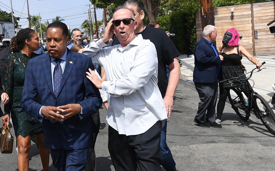 Larry Elder is escorted by a security guard on Wednesday, Sept. 8, 2021, in Venice, Calif., after a woman in a gorilla mask, at right, threw an egg at him.