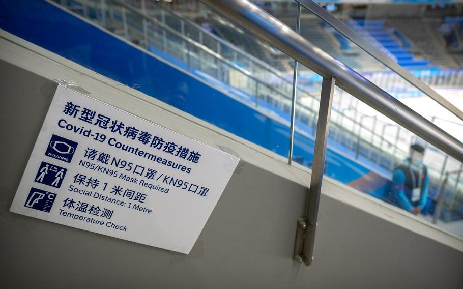 A staff member stands near a sign outlining COVID-19 protection measures during the Experience Beijing Ice Hockey Domestic Test Activity, a test event for the 2022 Beijing Winter Olympics, at the National Indoor Stadium in Beijing, on Nov. 10, 2021.