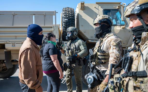Federal immigration agents speak to two people.