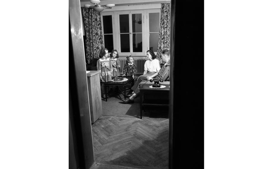 A vertical, black and white photo of a family seated on a couch in a living room.