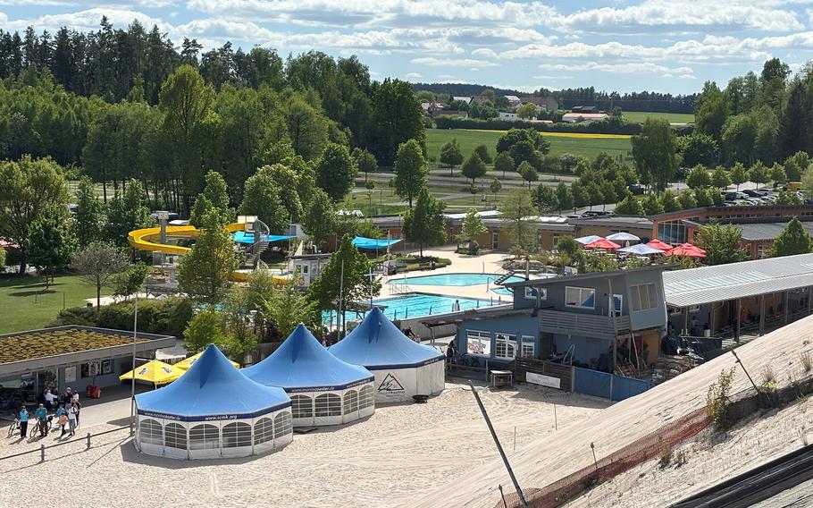 A water park featuring multiple swimming pools and a waterslide is shown from a nearby hilltop.