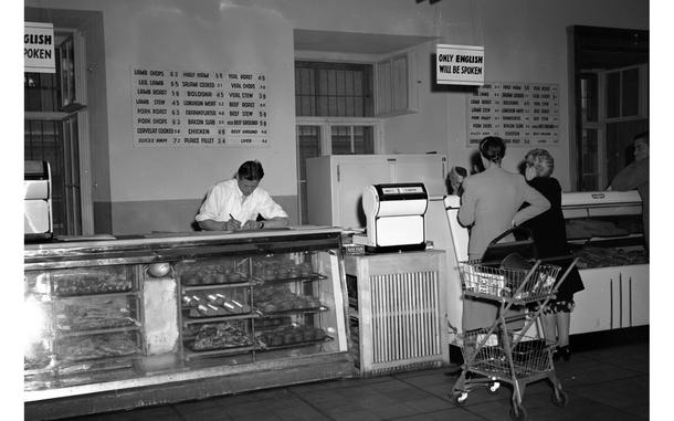 A black and white photo of a meat section at a commissary, with two women standing in front of a counter.