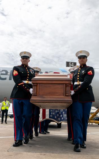Marines carry a casket on the runway of an airport.
