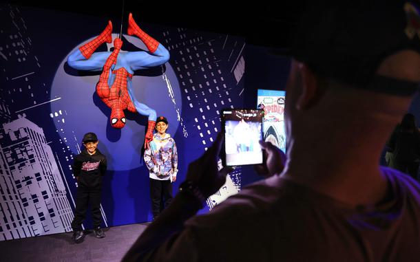 People pose next to a life-size Spider-Man statue or mannequin. 