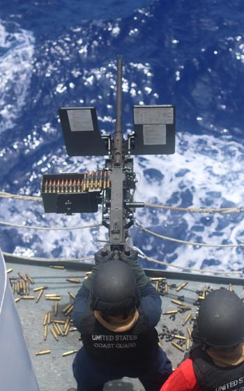 Coast Guard members shoot a machine gun.