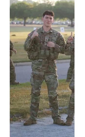 A soldier posing for a photo pointing up with the index finger on his right hand.