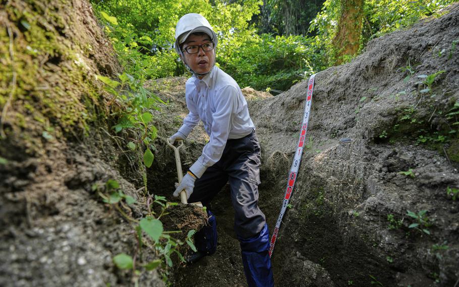 A man in a hard hat digs between rocks in a forest.