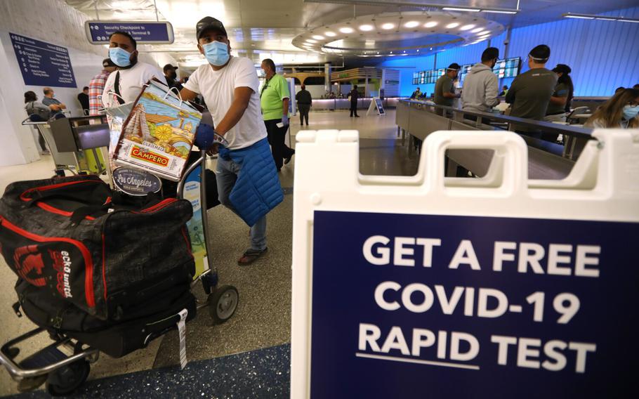 Arriving travelers walk past a sign directing them to get a free COVID-19 Rapid Test at the Tom Bradley International Terminal at Los Angeles International Airport, Dec. 3, 2021. 