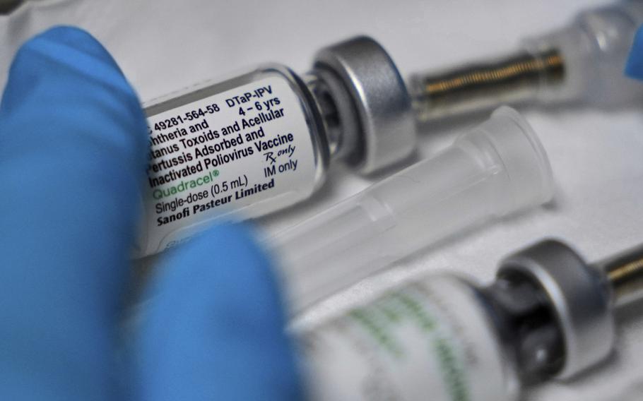 A hand wearing a blue glove touches two vaccine bottles.