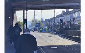 Pedestrians walk down a street in the area in London where police say a man wielding a sword attacked members of the public and two police officers on Tuesday, April 30, 2024 in the east London community of Hainault.