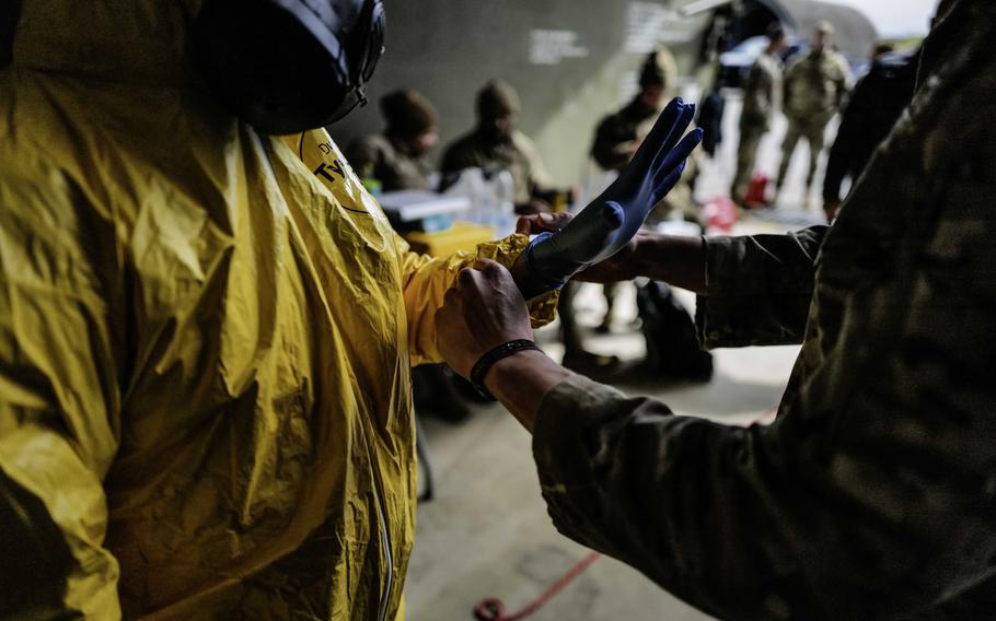 Staff Sgt. David Gogev, a plans and operations specialist with the 52nd Civil Engineer Squadron, right, assists an airman in donning protective gloves as part of a radiological detection and decontamination exercise April 24, 2024, at Spangdahlem Air Base, Germany. The exercise emphasizes hands-on training in safety and contamination prevention techniques.