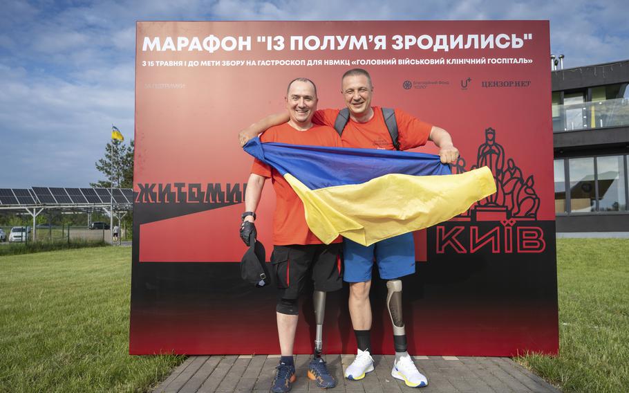 Serhii Khrapko, left, and Oleksandr Shvetsov, both Ukrainian war veterans from 2014, display the Ukrainian flag after successfully completing a 75-mile walk to raise money for medical equipment in honor of their comrades wounded in Russia's war against their homeland, in Yuriv, Zhytomyr region, Ukraine, on Friday, May 19, 2023. They raised $84,000, short just the $14,000 needed to purchase a new gastroscope for Ukraine's National Military Medical Clinical Center.