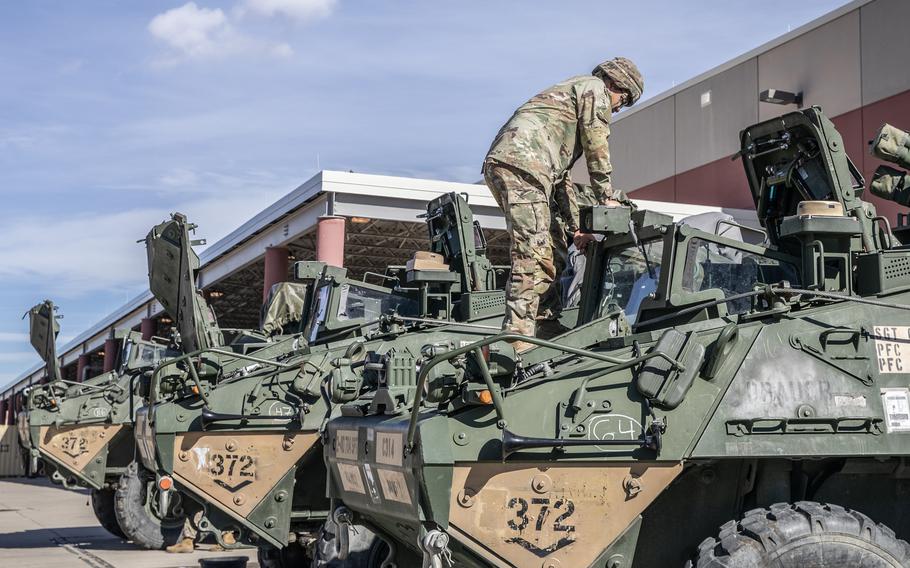 A soldier stands on a Stryker as he prepares to climb into it.