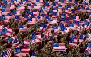A mass of flags being held up by uniformed soldiers in berets.