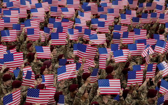 A mass of flags being held up by uniformed soldiers in berets.