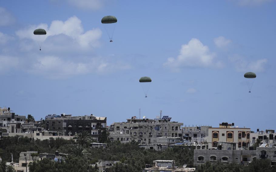 Crates attached to parachutes float to the ground, with a skyline of damaged buildings in the background.