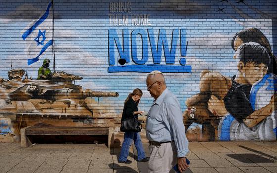 People walk past graffiti calling for the return of the hostages kidnapped during the Oct. 7 Hamas cross-border attack in Israel, in Kfar Saba, Israel, Thursday, Nov. 23, 2023. (AP Photo/Ariel Schalit)
