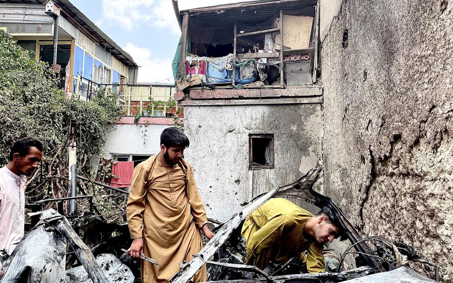 Men search the car hit by a drone strike that killed Afghan civilians in Kabul last summer.