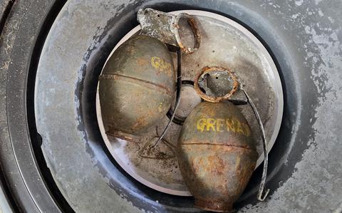 Two old, rusted hand grenades with yellow markings sit in a round metal container or bucket. 