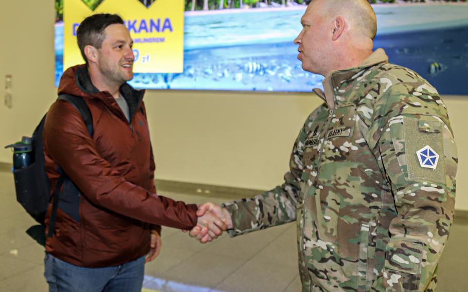 Command Sgt. Maj. Christopher Prosser, right, shakes hands with Sgt. Walter Malecki at the airport in Poznan, Poland, on Feb. 10, 2022. Malecki is the first active-duty  U.S. soldier to be assigned permanent change of station orders to Poland.