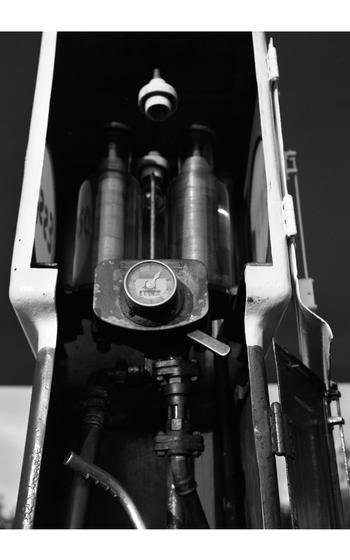A vertical, black and white photo of a pump at a gas station.