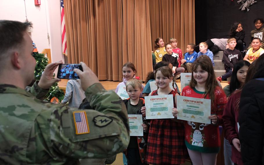 A parent in uniform takes a picture of a group of students holding placards.