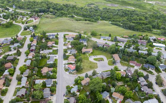 An aerial image of a small town neighborhood with a green space and park behind.