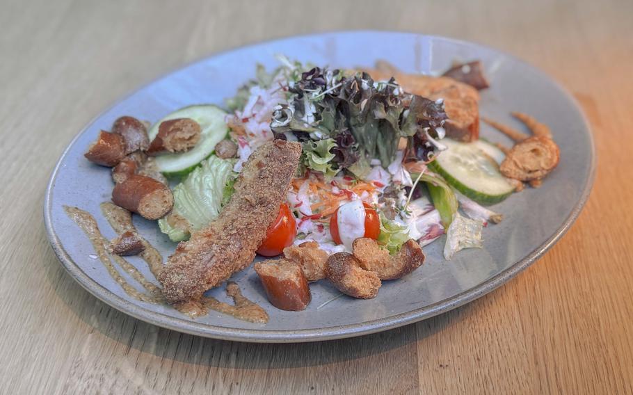 A breaded white sausage is served with sweet mustard and salty, crunchy pretzel croutons.