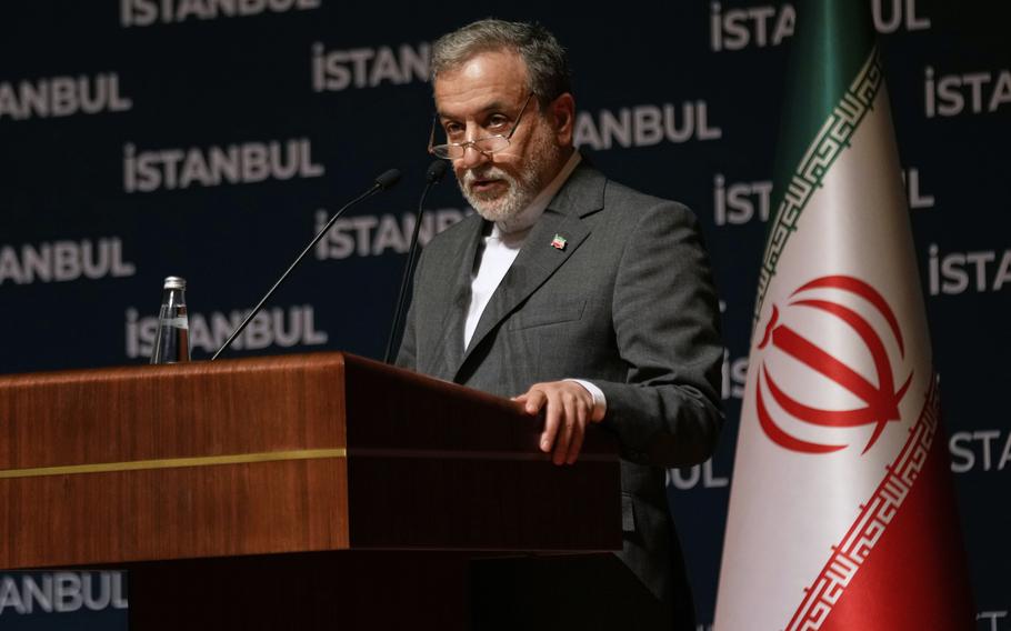 An Iranian government official wearing a gray suit and glasses stands at a podium and speaks into a microphone next to an Iranian flag and in front of dark backdrop with “Istanbul” printed in white letters.