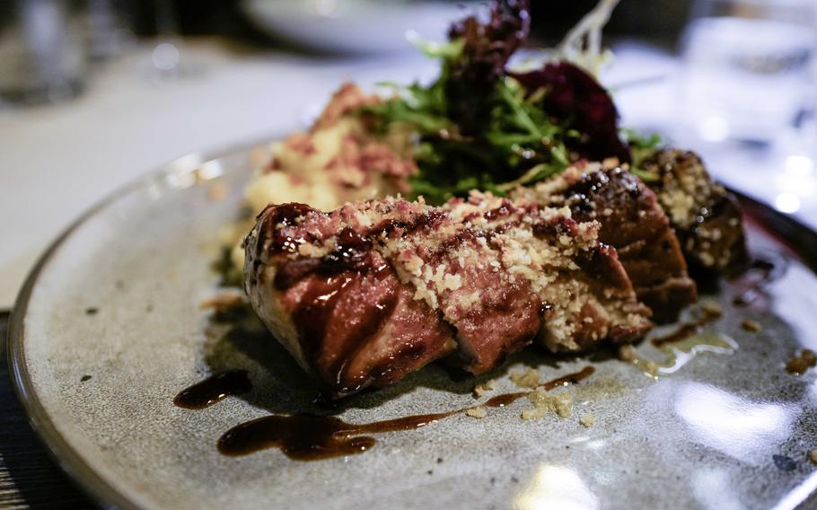 A tender pork fillet encased in a crispy herb crust, accompanied by parmesan potato puree and a wild herb salad dressed with a teriyaki glaze and onion crumble, as served at Grifo.