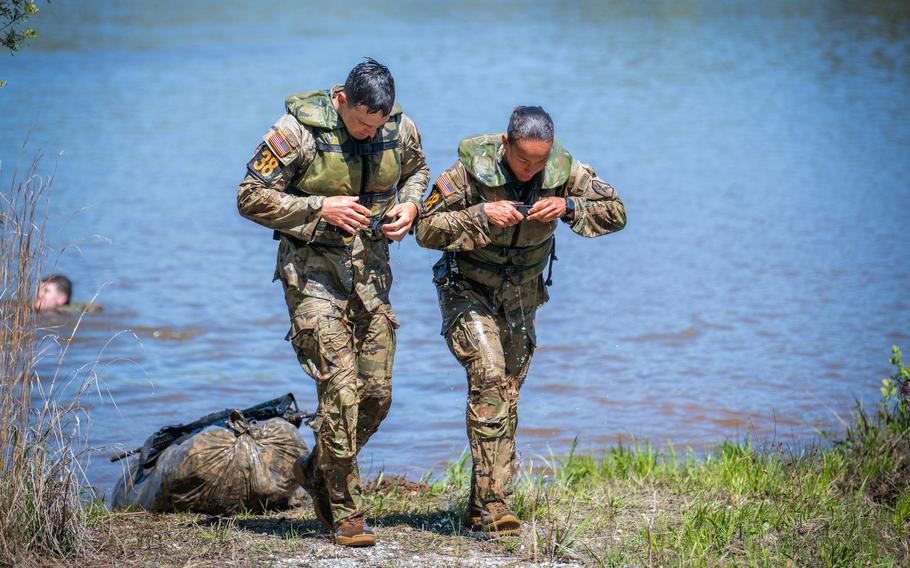 Two soldiers, one man and one woman, walk out of the water in uniform, still dripping wet.