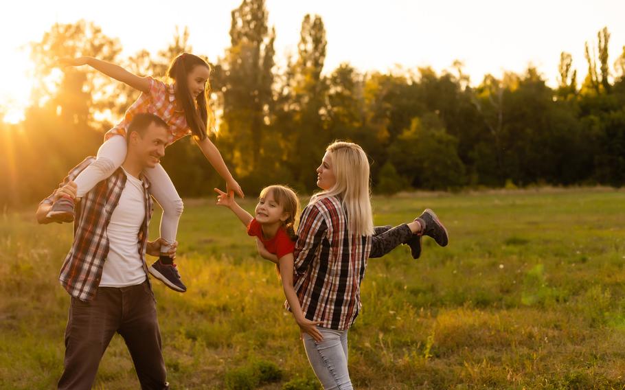A joyful family enjoys a sunny evening in a lush green field, with the children playfully engaged in imagination and laughter.