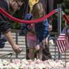 A young girl lays a white flower on the pile of flowers. A man next to her lays a pink flower.