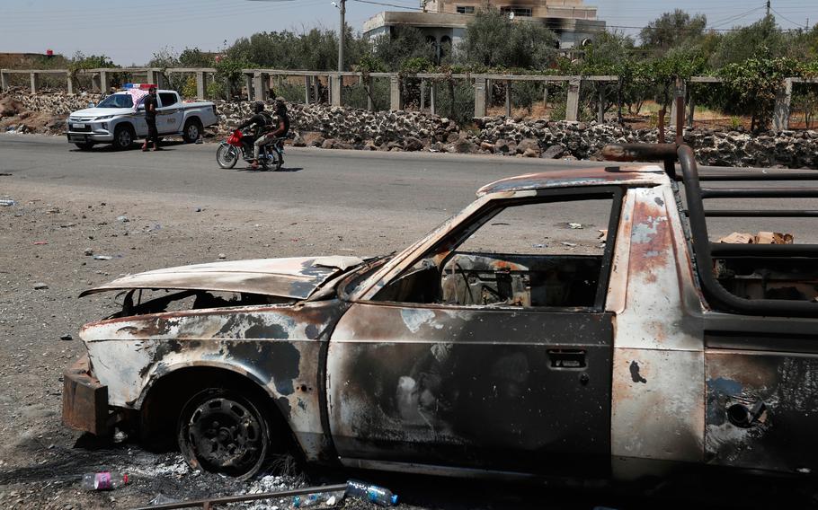 A burned-out vehicle at a security checkpoint.