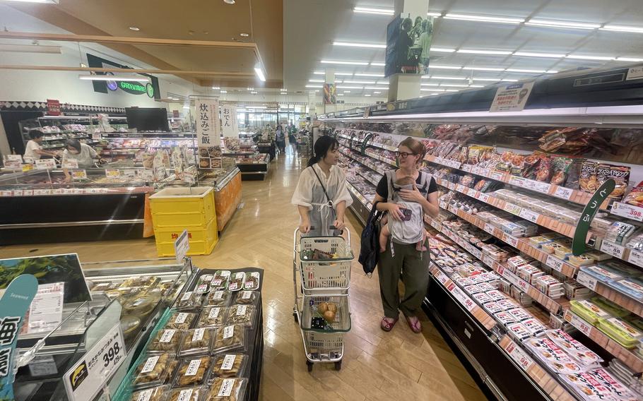 A member of the Japanese American Society shops with a Marine Corps spouse, who is carrying a baby, at a Japanese grocery store.