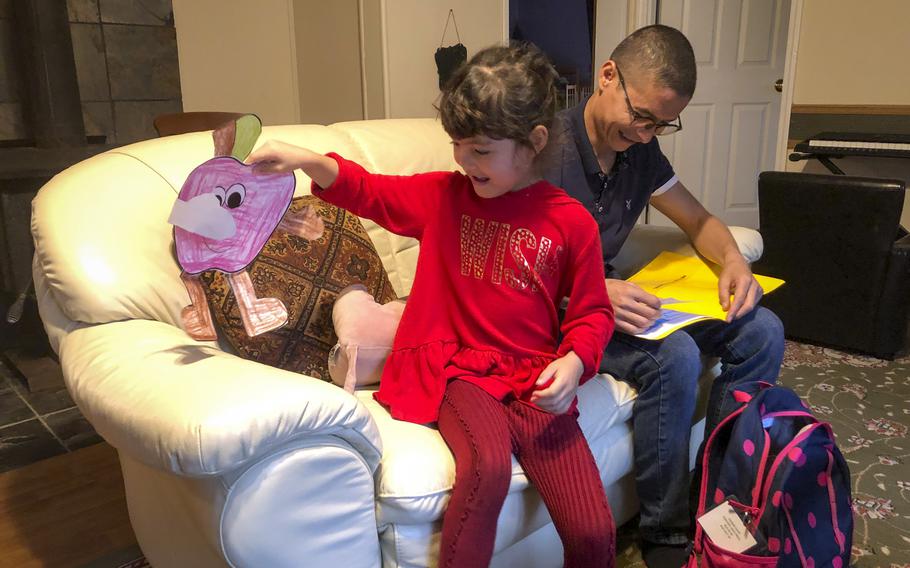 Zainab Asadi, 5, shows off some art she made while her father checks over what she did in school, at their home in the suburbs of Atlantic City, N.J., Oct. 26, 2021.