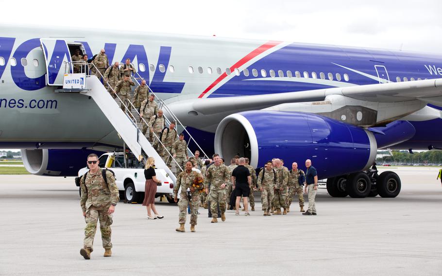 Soldiers in uniform walking down the steps of a plane and across the tarmac.