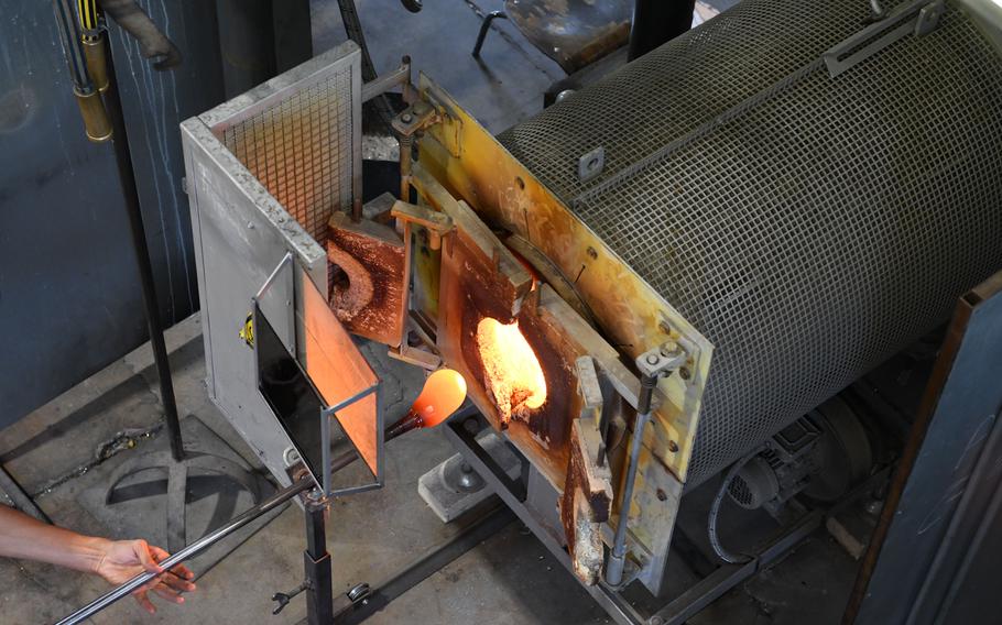 A hand inserts molten glass into a furnace.