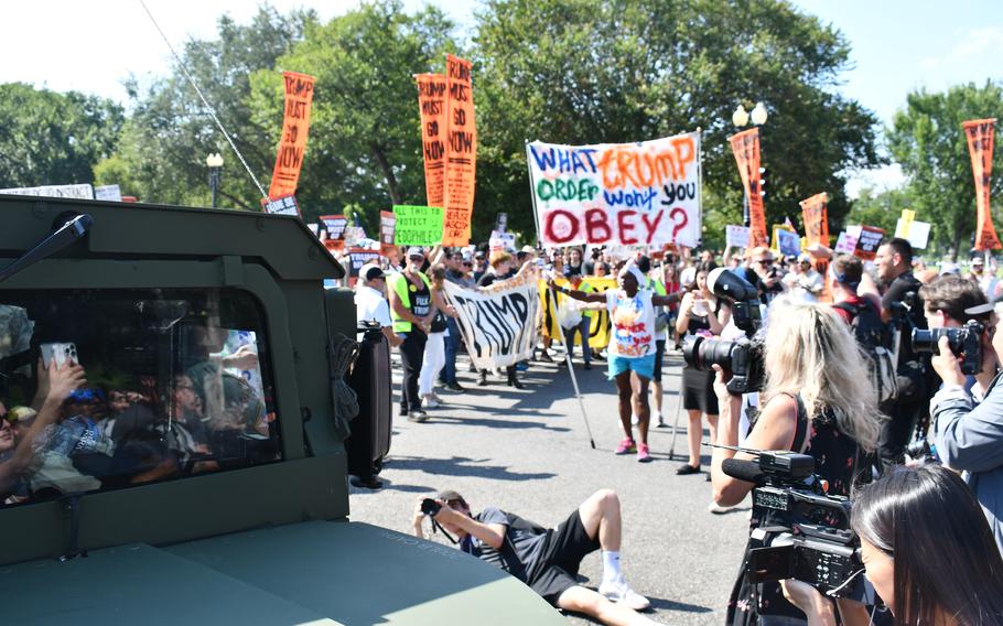 A crowd of protesters carrying signs opposing the Trump administration’s federal takeover of Washington, D.C., chant at National Guard members.
