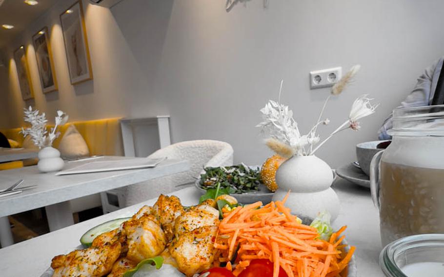 A generous portion of grilled chicken salad topped with fresh vegetables and creamy Caesar dressing, a healthy and flavorful choice at The Parlour breakfast boutique in Landstuhl, Germany. The owner’s family motto, “It is OK to eat cake for breakfast,” adorns the wall.