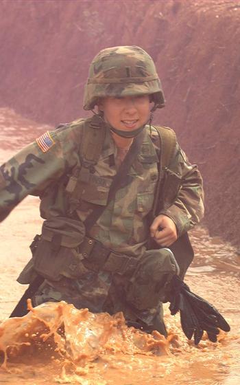 A vertical photo of a soldier wading through muddy water.
