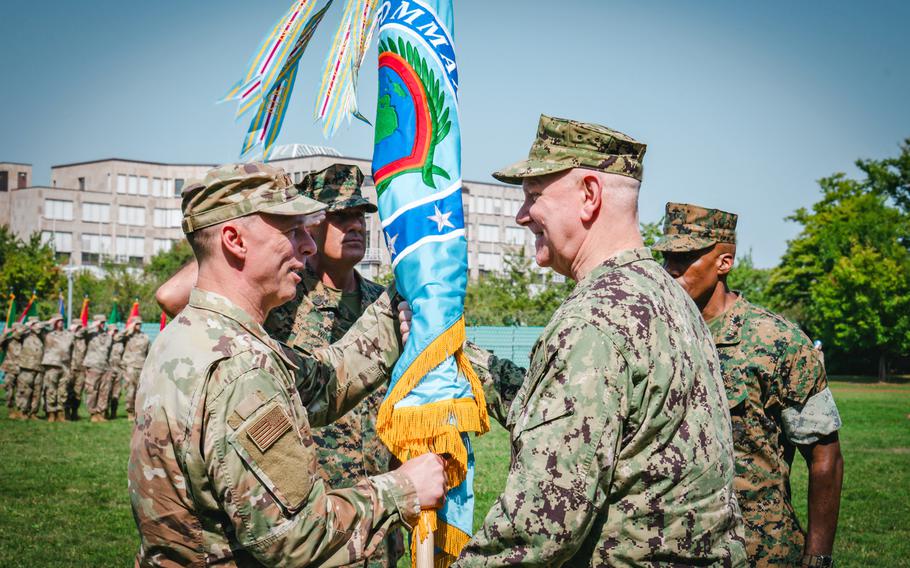 An Air Force general receives the flag from a Navy admiral during a change of command.