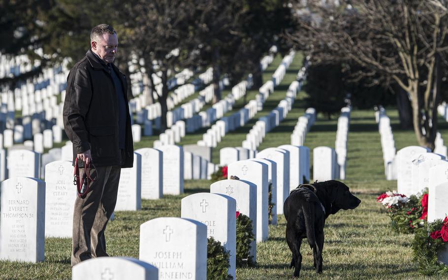 Retired Marine Col. Barry Neulen looks at the headstone of his father-in-law, Korean War veteran Lester Lazarus during an annual wreath-laying event at Arlington National Cemetery on Saturday, Dec. 17, 2022. Accompanying Neulen is his service dog, Frankie. Tens of thousands of volunteers helped Wreaths Across America place some 257,000 wreaths on the headstones at Arlington on Saturday.