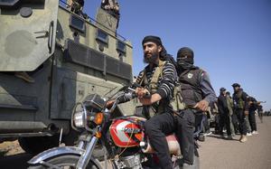 Two men ride a motorcycle next to an armored vehicle.