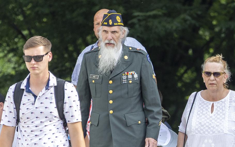 People walking including an older man with a long beard wearing an Army uniform and a veterans hat.