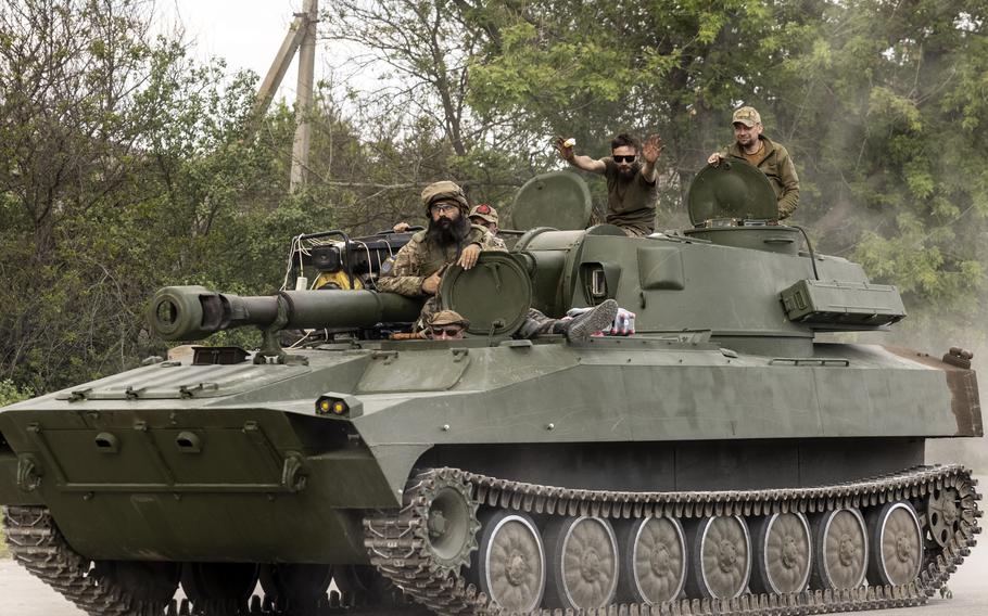 Ukrainian soldiers ride on an armored vehicle, an old Soviet-designed 2S1 self-propelled howitzer, as one soldier raises a vanilla ice cream cone, in the Zaporizhzhia region on May 20, 2023. 