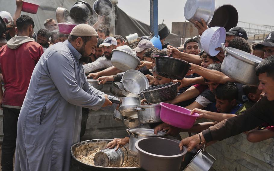 A row of children hold out buckets and pots to receive food.