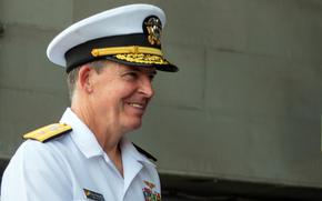 A naval officer in white dress uniform and hat is seen from the side.